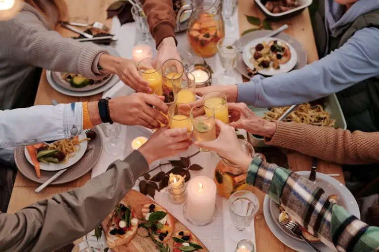 From above of crop friends enjoying dinner with candles while cheering with glasses of drinks